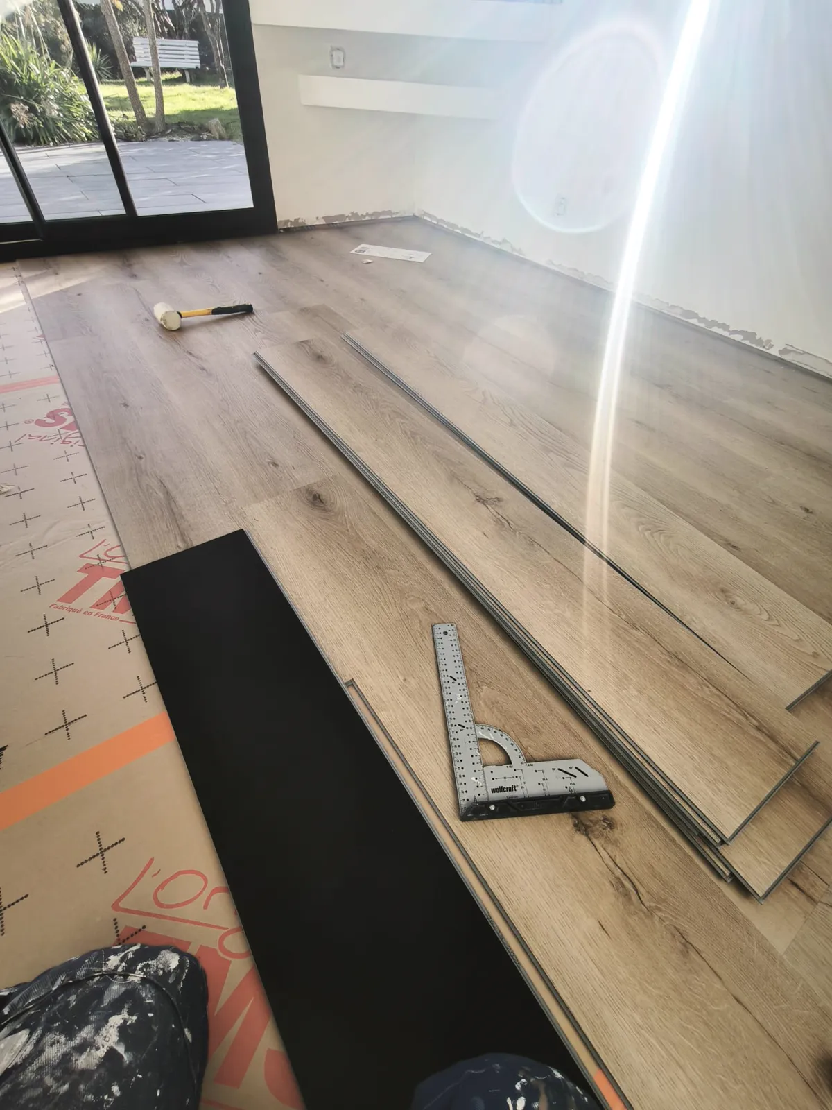 Pose d'un parquet en cours, lames et équerre devant une baie vitrée